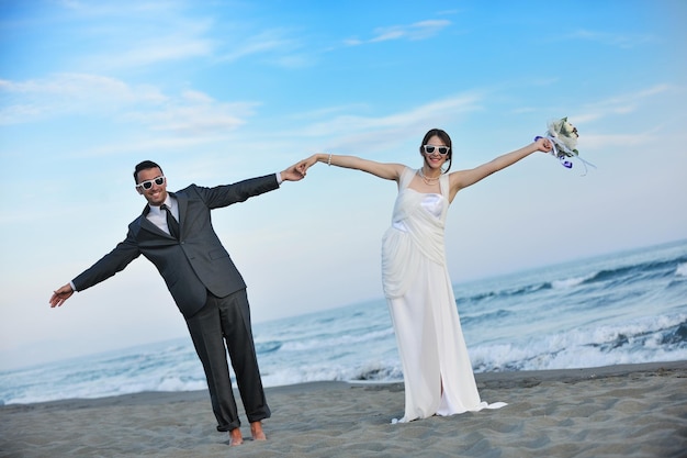 幸せなちょうど結婚した若いカップルを祝って、美しいビーチの夕日を楽しんでください