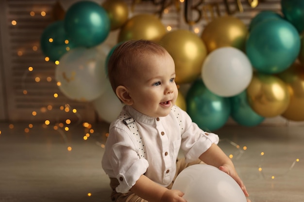 A happy kid on the background of balloons with garlands celebrates his birthday