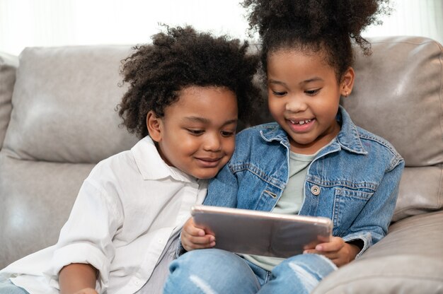 Happy kid boy and girl with afro hair play tablet in home