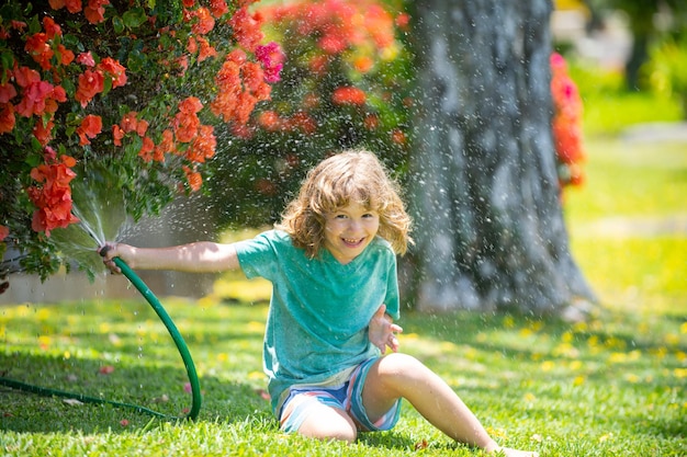 幸せな子供の男の子は、庭の家の園芸で花に水をまくホースの子供から水を注ぐ