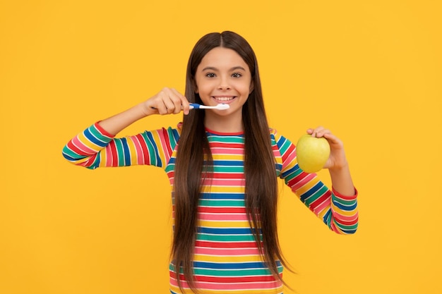 Happy kid brush teeth with toothbrush holding apple yellow background strong teeth