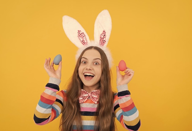 Happy kid in bunny ears and bow tie hold easter eggs on yellow background