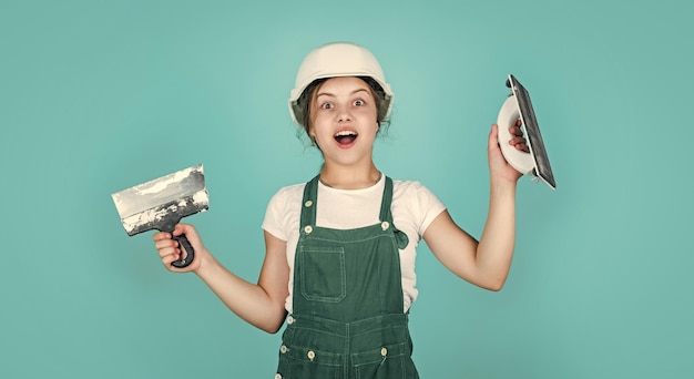 Happy kid engineer with plastering tool spatula in hard hat development