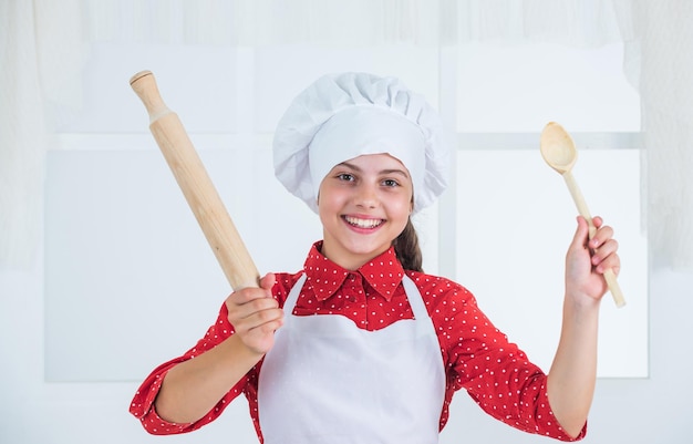 Happy kid girl in cook hat and apron in kitchen chef