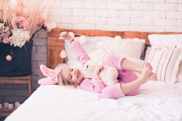 Happy kid girl having fun with teddy bear in bed