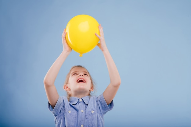 Happy kid girl holds up yellow balloon isolated on blue background copy space