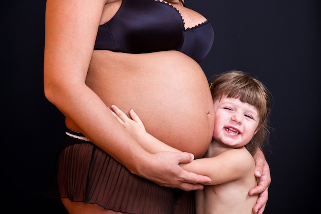 Ragazza felice del bambino che abbraccia la pancia della madre incinta