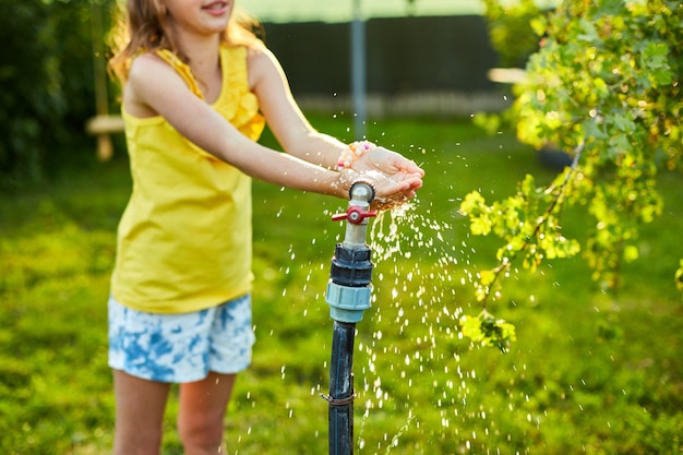 Happy kid girl playing by hand with garden sprinkler