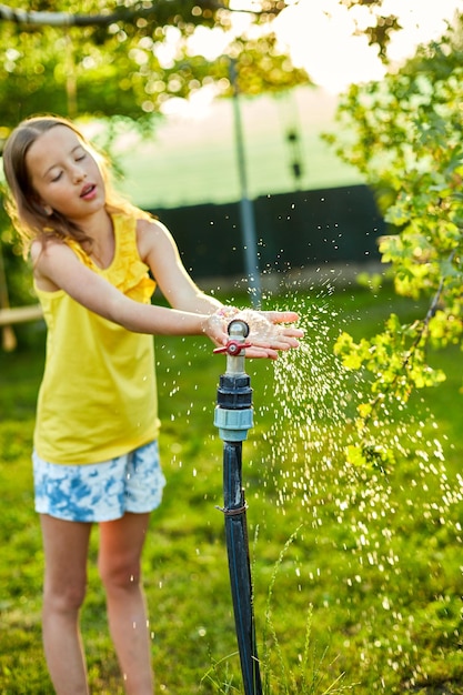 庭のスプリンクラーで手で遊んで幸せな子供の女の子