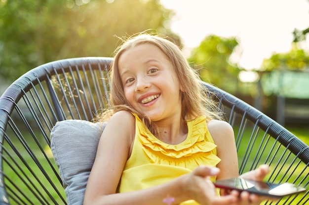 屋外の公園で携帯電話でゲームをしている幸せな子供の女の子