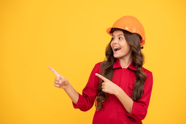 Happy kid girl in protective helmet pointing finger on copy space for advertisement good offer