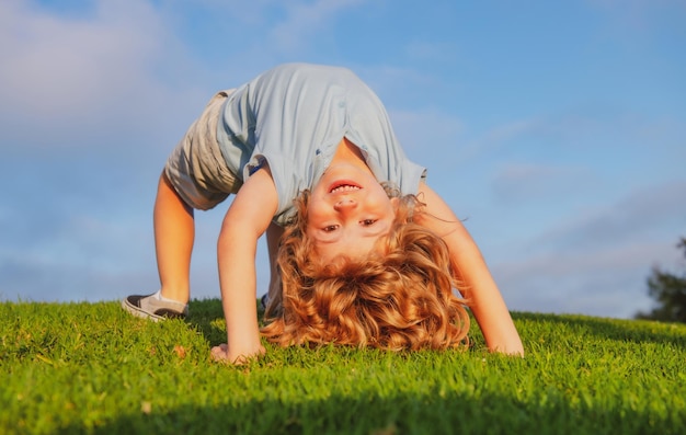 Happy kid girl standing upside down on her head on grass in summer day