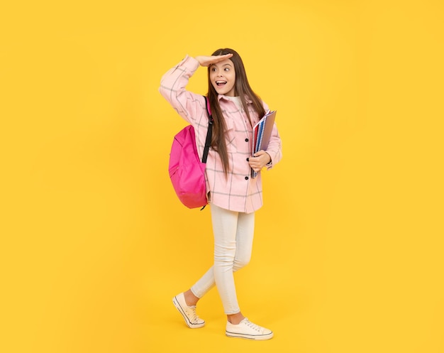 Happy kid girl wear pink checkered shirt carry school bag and notebooks, hello.