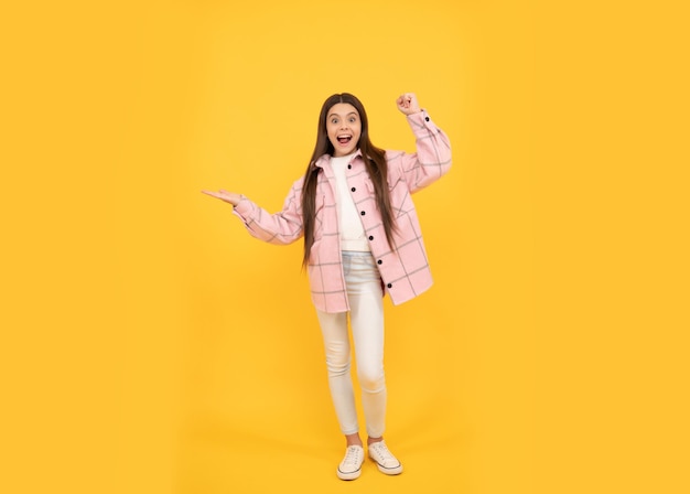 Happy kid girl wear pink checkered shirt presenting product copy space promoting