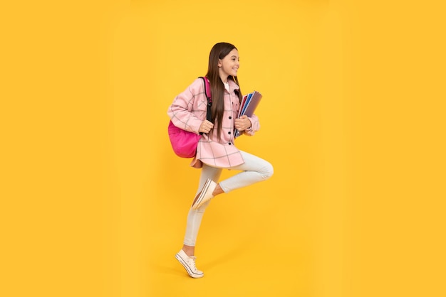 Happy kid girl wear pink checkered shirt running with school bag and notebooks, hurry up.