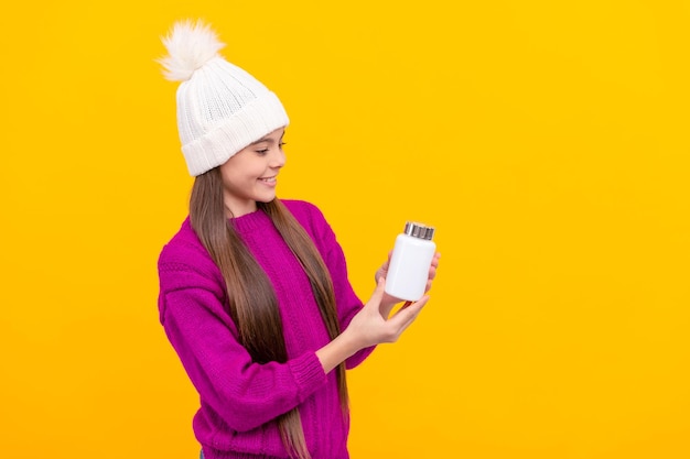 Happy kid in hat looking at vitamins on yellow background health