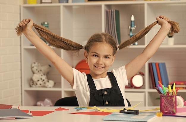 Bambino felice che si diverte con la coda di cavallo dei capelli lunghi alla lezione scolastica nella scuola dell'uniforme dell'aula