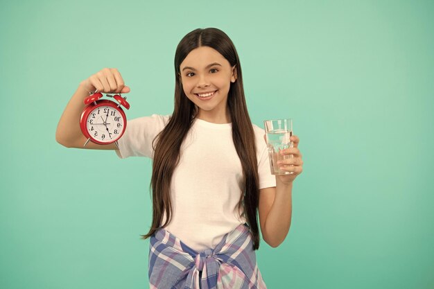 Happy kid hold glass of water and clock to stay hydrated and keep daily water balance thirst