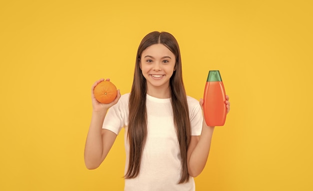 Happy kid hold hair conditioner bottle and grapefruit on yellow background cosmetic