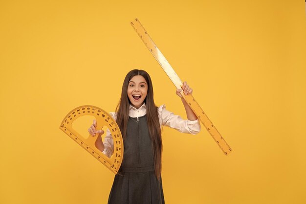 Happy kid hold math protractor and ruler in school on yellow background education