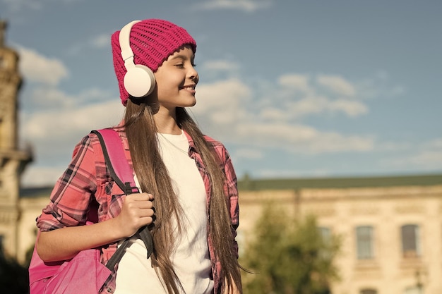 Happy kid listen to music playing in modern headphones traveling around city outdoors technology