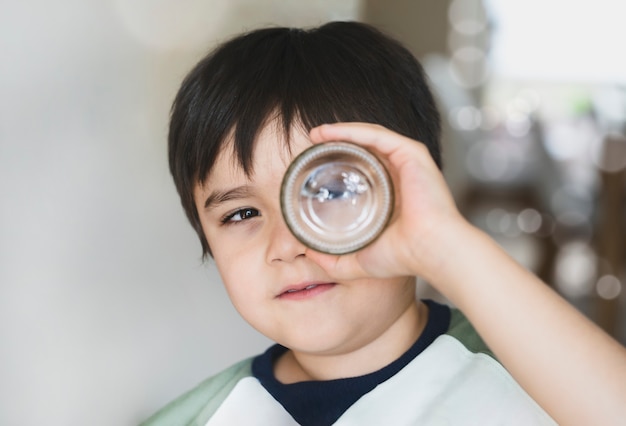 Happy kid looking through glass jar. Child boy having fun playing with DIY toy at home