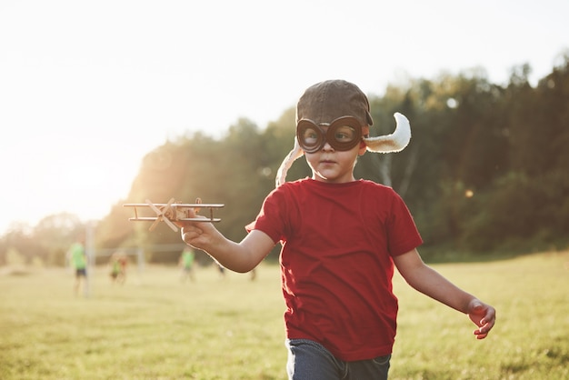 Happy kid in pilot helmet playing with a wooden toy airplane and dreaming of becoming flying