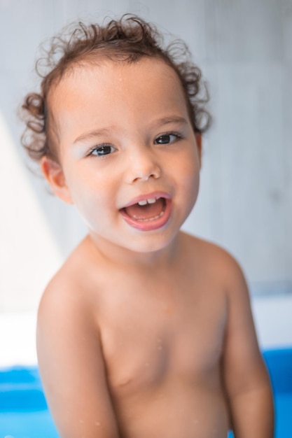 Счастливый ребенок играет в надувном бассейне на заднем дворе Кудрявый малыш улыбается и играет с водой