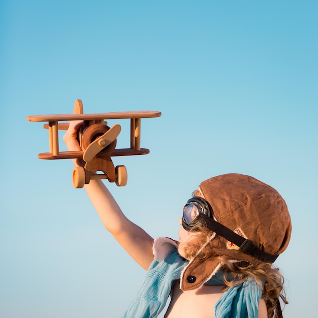 Foto bambino felice che gioca con l'aeroplano giocattolo su sfondo blu cielo estivo