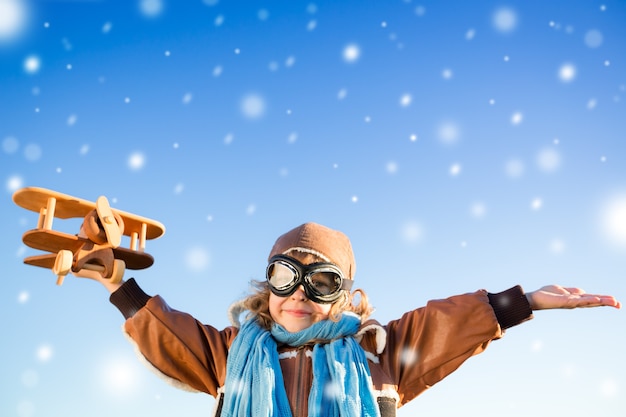Счастливый ребенок играет с игрушечным самолетиком на фоне голубого зимнего неба