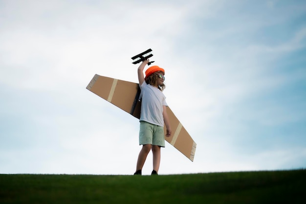 Happy kid playing with toy paper wings outdoors in summer field Travel and kids vacation concept Imagination and freedom