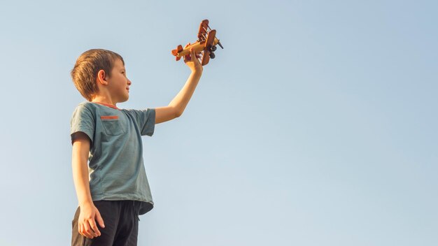 Happy kid playing with toy wooden airplane against sky background