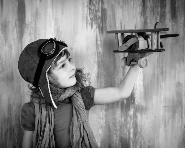 Happy kid playing with toy wooden airplane indoors. Black and white photo