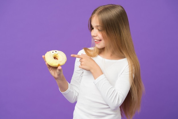 Happy kid point finger at donut on violet background little girl with glazed ring doughnut on purple backdrop unhealthy eating child smile with junk food food and dessert childhood and childcare