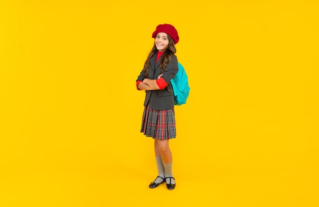 Счастливый ребенок в школьной форме с беретом и рюкзаком на желтом фоне моды