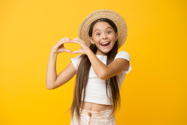 Happy kid show heart gesture she love summer vacation spring fashion for kids childhood happiness cheerful little girl wear straw hat ready for beach party small beauty