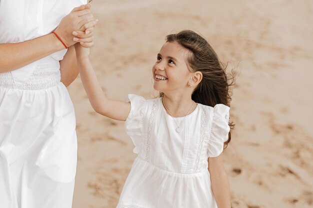 happy kid smiling and holding hand of crop mom on sandy seashore