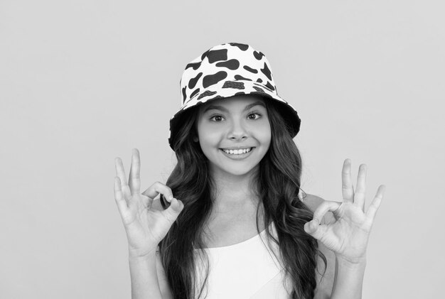 Happy kid in summer bucket hat has curly hair on yellow background ok