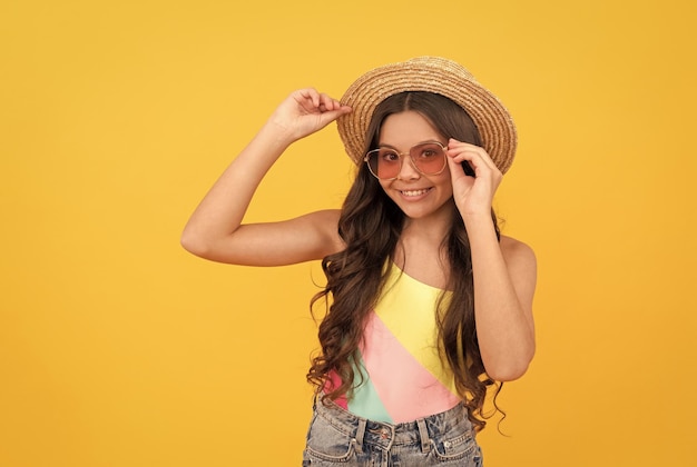 Happy kid in summer straw hat and glasses has curly hair on yellow background summer fun