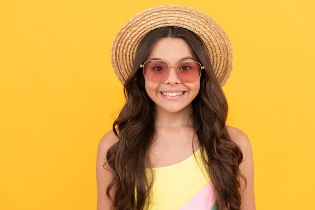 Happy kid in summer straw hat and glasses has curly hair on yellow background summer mood