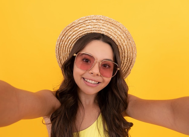 Happy kid in summer straw hat and glasses making selfie on yellow background summer selfie