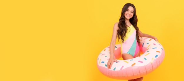 Happy kid in swimming suit with doughnut inflatable ring on yellow background Banner of summer child girl in swimsuit studio poster header with copy space