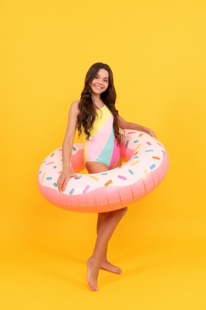 Happy kid in swimming suit with doughnut inflatable ring on yellow background childhood