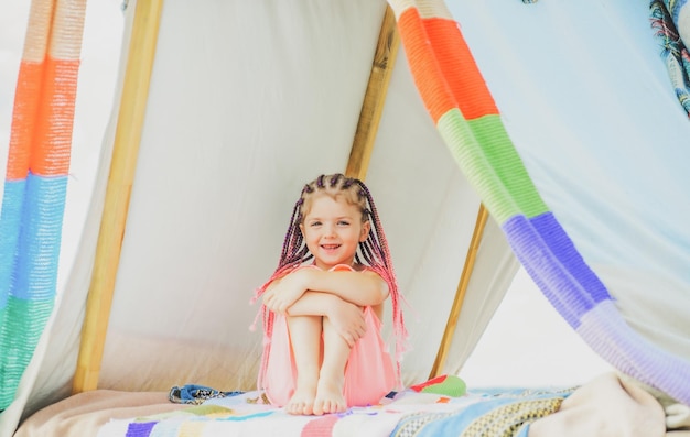 Happy kid with dreadlocks play in tent Child camping concept Girl playing in camp Having fun outdoor