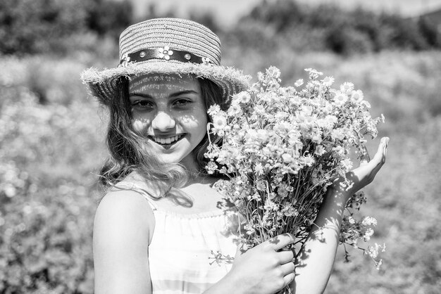 Happy kid with healthy baby skin smile with chamomile flowers natural floral spa and beauty care in sun hat on sunny summer landscape skincare