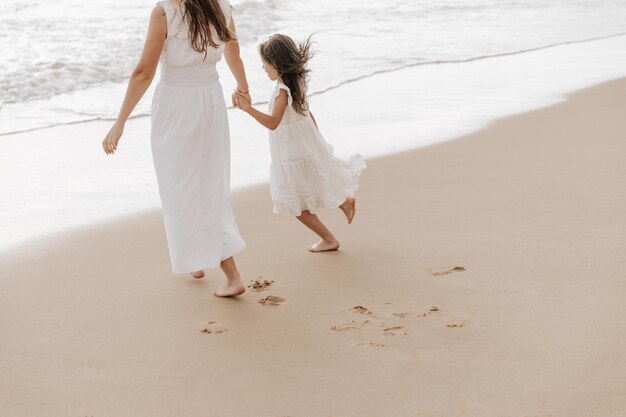 happy kid with mother holding hands and strolling on sandy seashore
