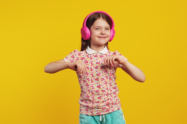 Happy kid with pink headphones listening music and dancing against yellow