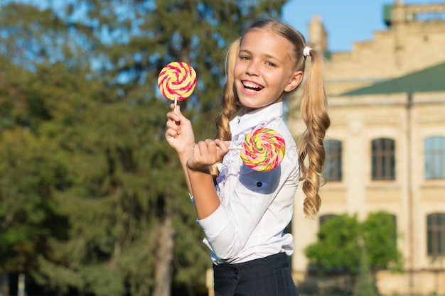 Happy kid with sweet candy Happy childhood Kid child holding lollipop candy Sweets and dessert concept Happy kid with candy outdoors having fun Schoolgirl relaxing on sunny day School nutrition