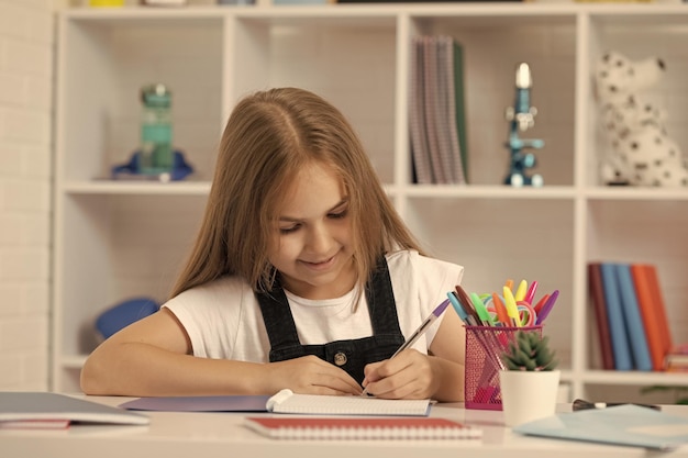 Happy kid write in workbook at school lesson in classroom wear uniform knowledge