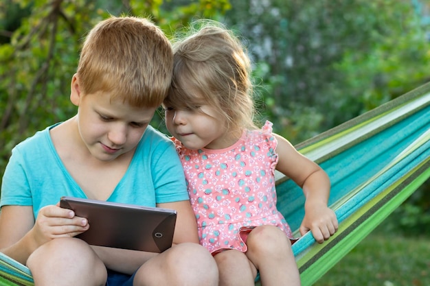 사진 야외 공원에서 해먹에 앉아 디지털 태블릿을 사용하여 행복한 아이들 소년과 소녀